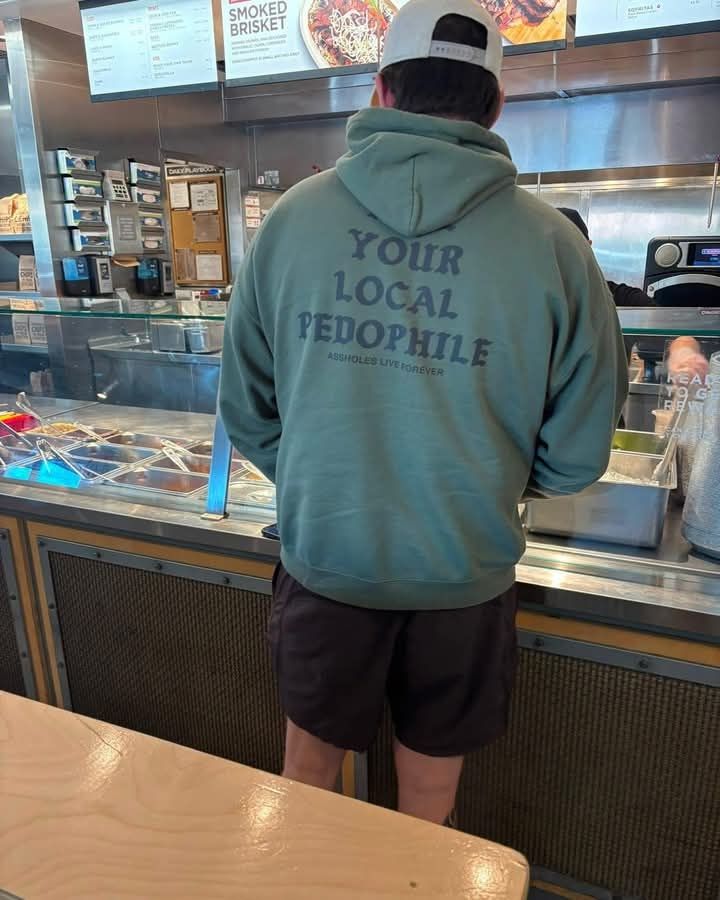 A man in shorts and a hoodie stands at the counter of a restaurant.

The hoodie reads "Kill Your Local Pedophile" but the hood is covering the 'Kill' portion
