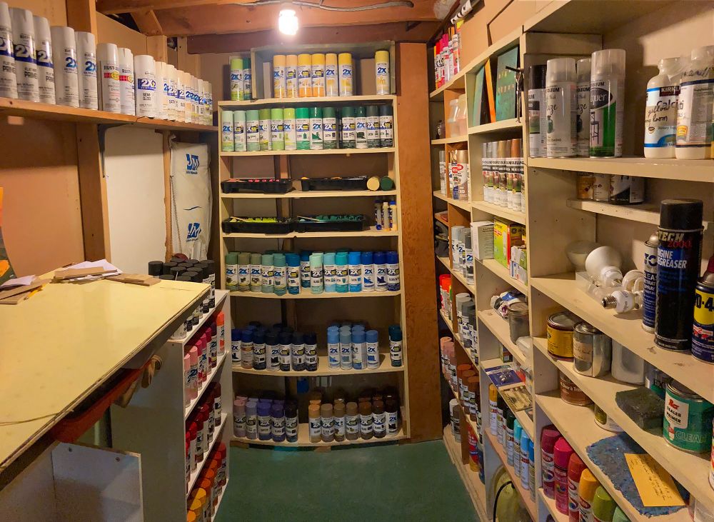 A basement alcove mostly filled with several hundred spray paint cans in every shade.