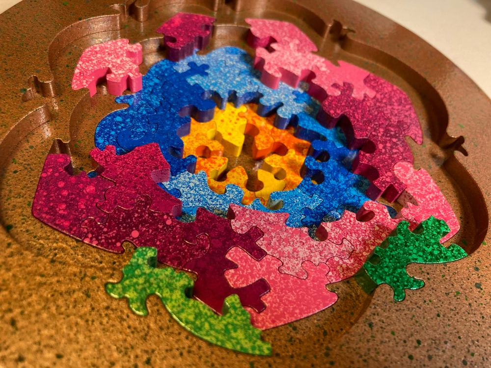 A colorful handmade wooden puzzle with multiple layers depicting an abstract flower design, in the midst of assembly 