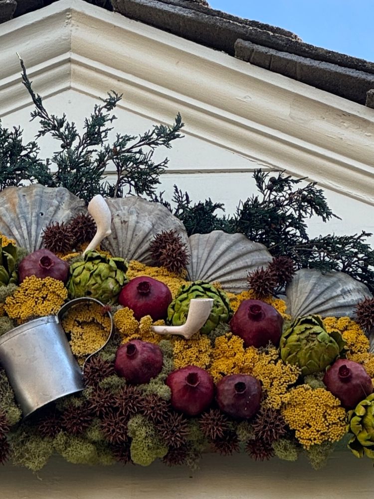 Closer view of garland with fossil shells, pomegranates, flowers, foliage, bone pipes & a tin cup.