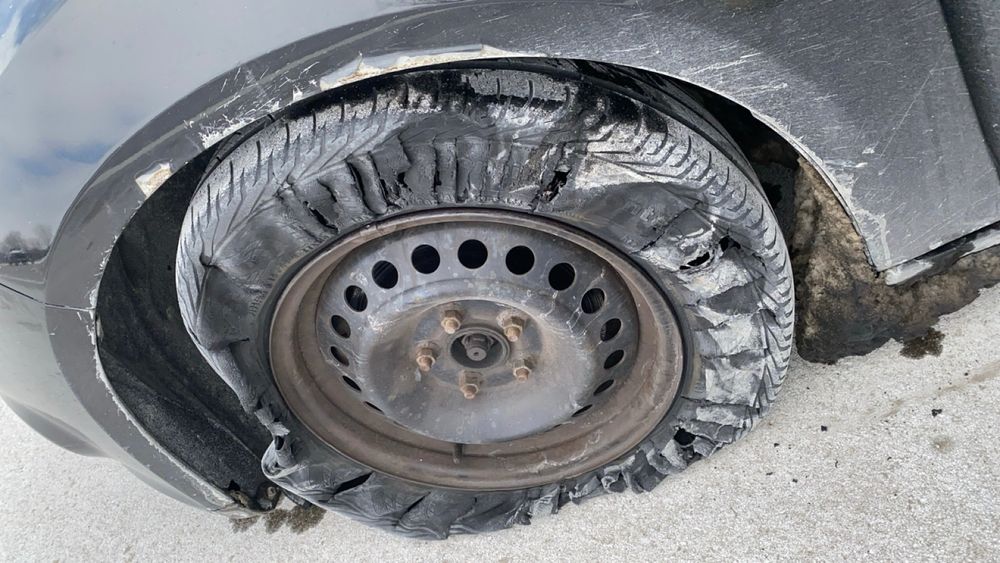 A picture of a tire on a black car that is not just flat but shredded missing its hubcap.