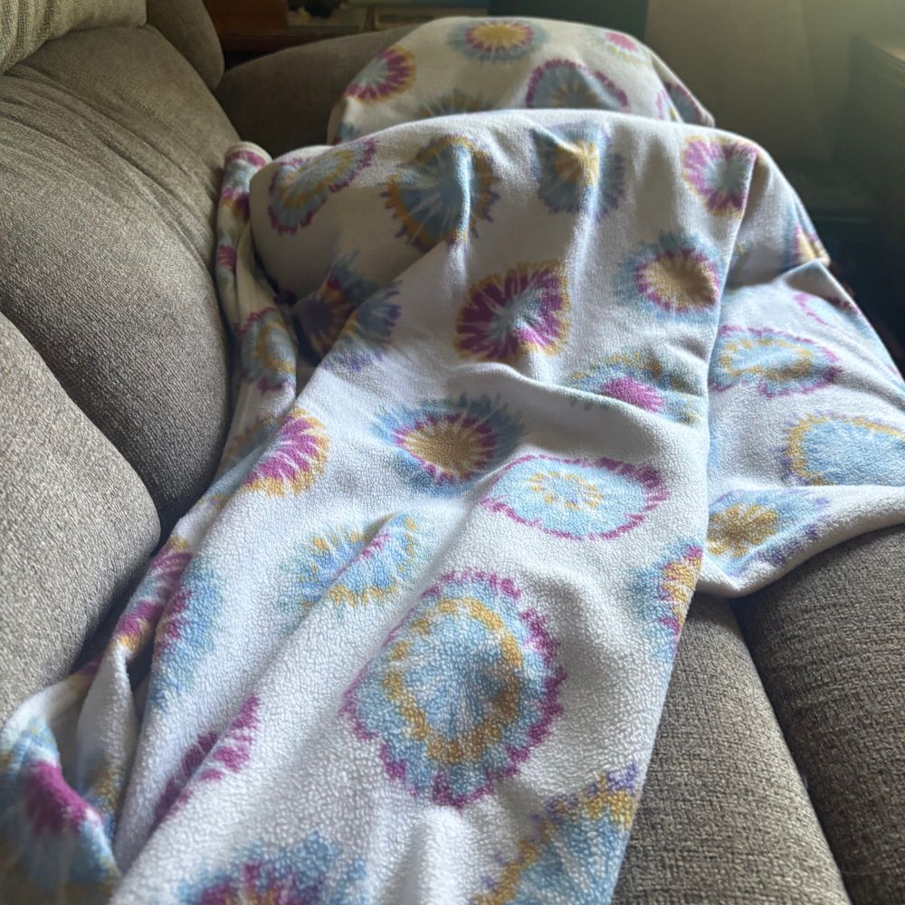 A lump under a tie dye fleece blanket. 