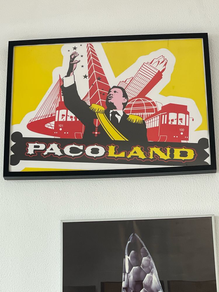 Imagen de una pared en la que está colgada, en un marco negro, la ilustración de Álvaro Valiño “Pacoland”