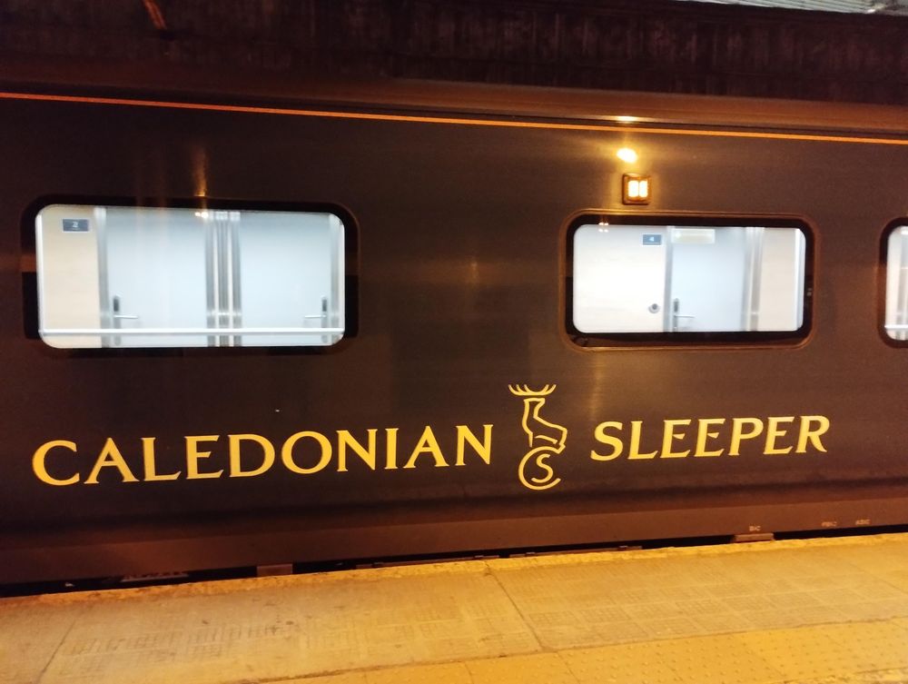 Wagen mit erleuchteten Fenstern vom Gleis, Aufschrift: Caledonian Sleeper