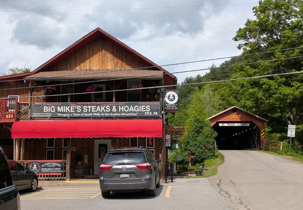 A cheesesteak shop next to a red covered bridge.