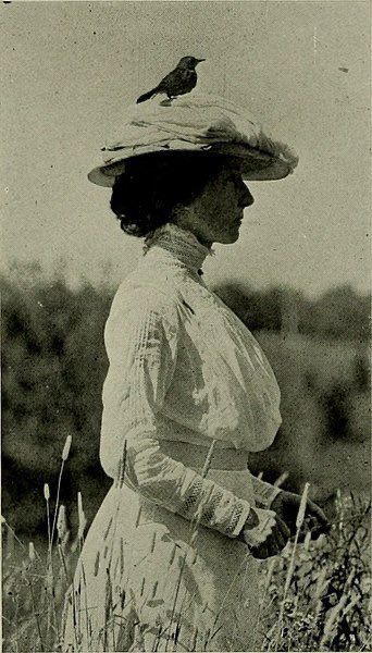 Vintage photo of woman in field with bird perched on her hat.