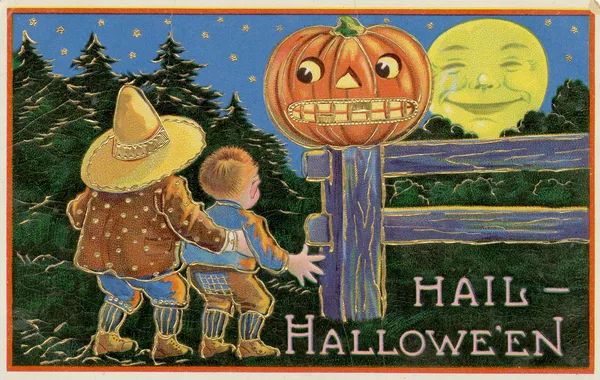 Vintage Halloween postcard. ‘Hail Halloween’ Two children look up in fear at a grinning pumpkin on a fence and a smiling moon, star-filled sky and forest in distance. 
