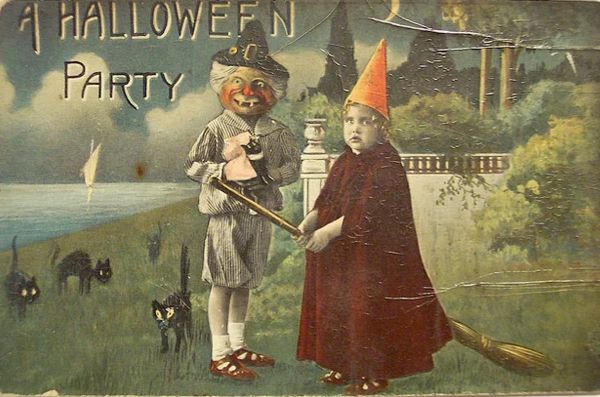 Vintage Halloween card with black cats, pumpkin headed child and strange child witch perched on a broomstick with red cloak and orange hat, at the top it says A Halloween Party. See in a lakeside / country garden style landscape.