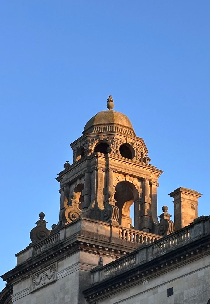 Photo of portion of the roof and tower of the Guildhall.
An open-air belfry or cupola with arched openings and decorative carvings. A small dome topping the structure, crowned with an ornamental finial. Detailed stonework along the roofline, including balustrades and scroll-like accents.