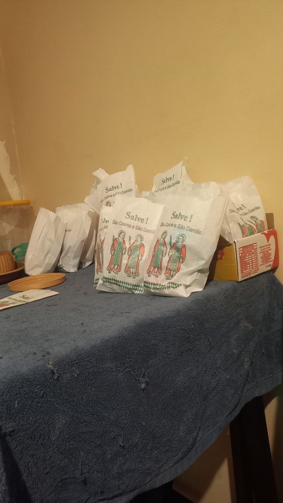 Saquinhos de doce de Cosme e Damião em cima de uma mesa sobre uma toalha azul.