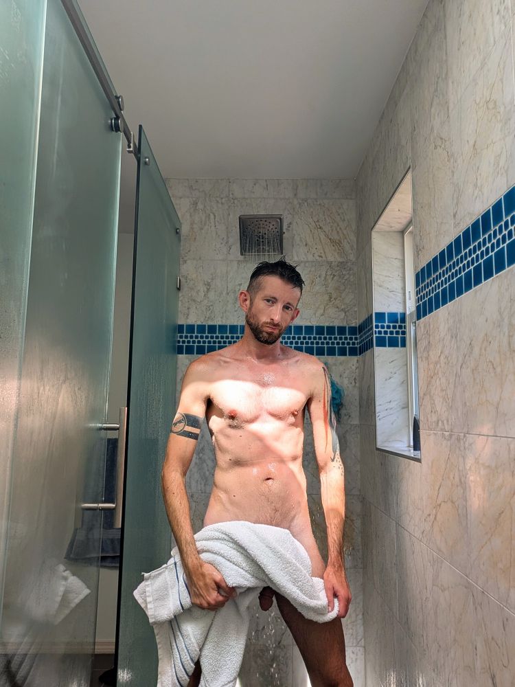 Man standing in shower holding a towel. He's being subtle, but also not subtle. 