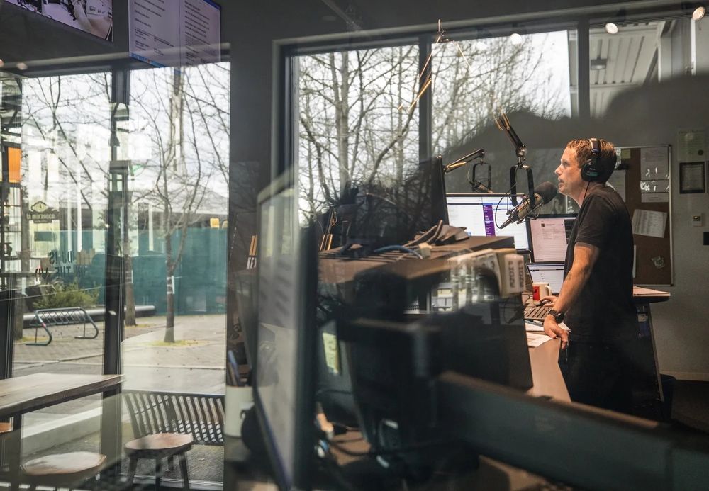 KEXP morning show host John Richards works in the station’s main DJ booth as an empty Seattle Center courtyard is reflected in the window. (Steve Ringman / The Seattle Times, 2020) 