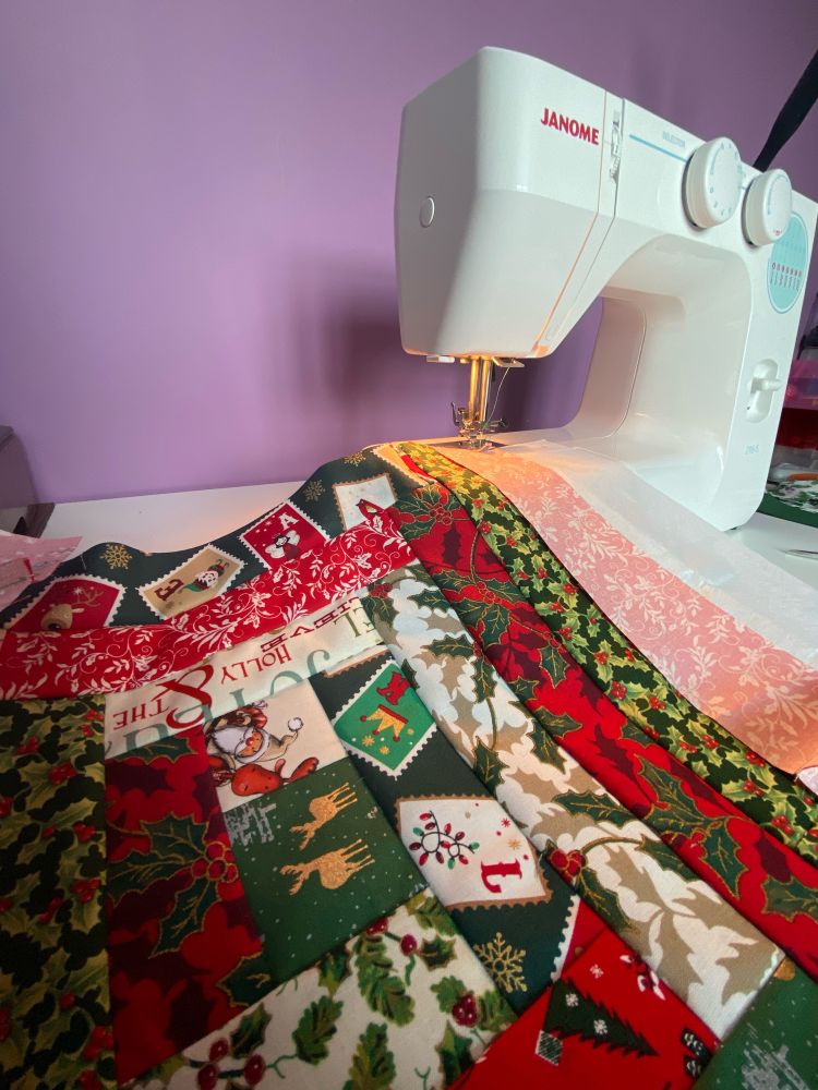Strips of Christmas fabric being sewn together on a Janome sewing machine to make a Christmas stocking. 