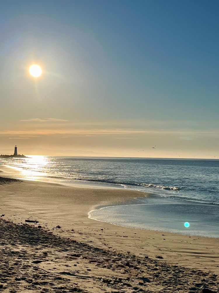 High tide as the morning sun hits Monterey Bay. A lighthouse in the distance. 
