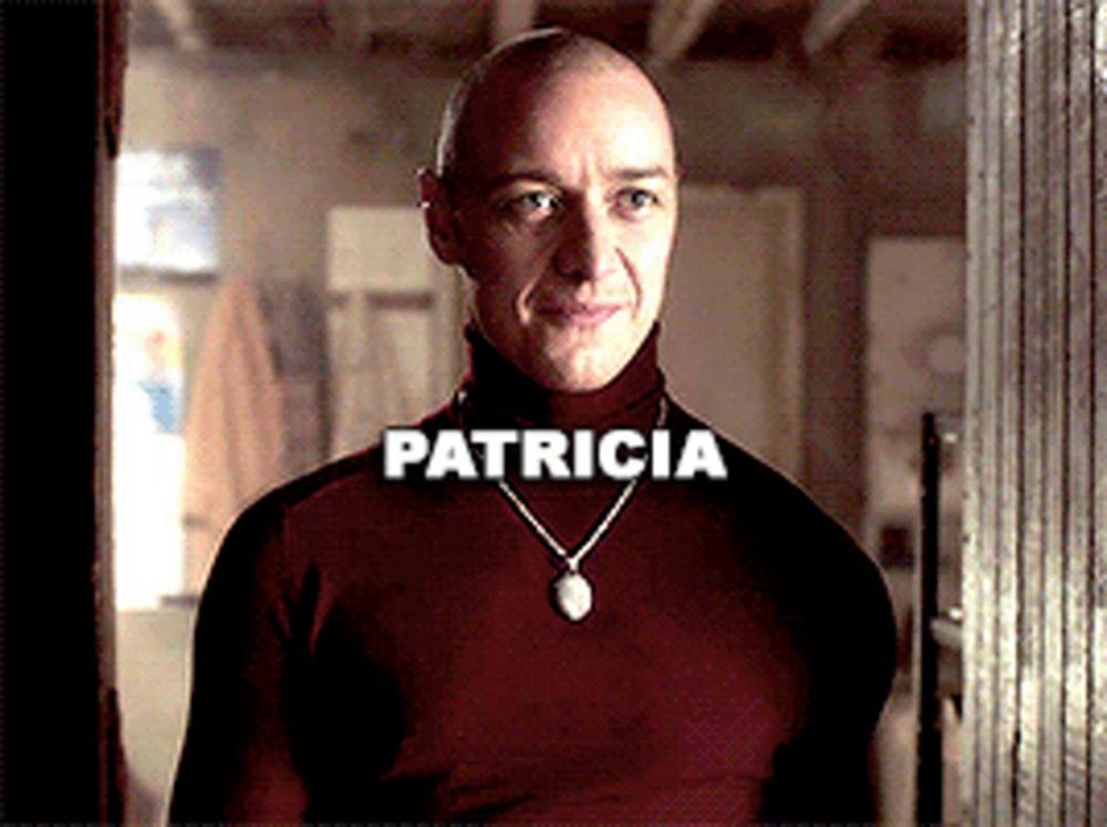 a bald man wearing a red turtleneck and a necklace with the name patricia written on it