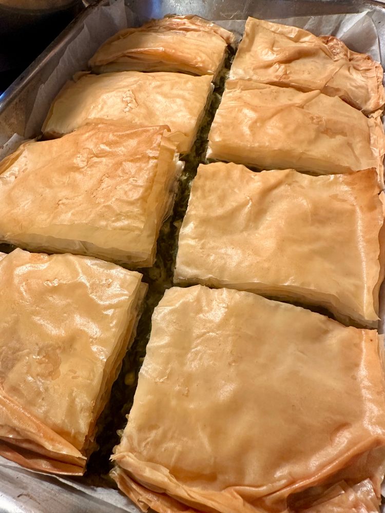 Rectangular pan filled with Greek spanakopita (spinach pie) cut into eight pieces. 