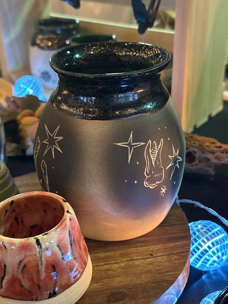 Wheel thrown vase with a black glitter glaze and carved teeth and stars.