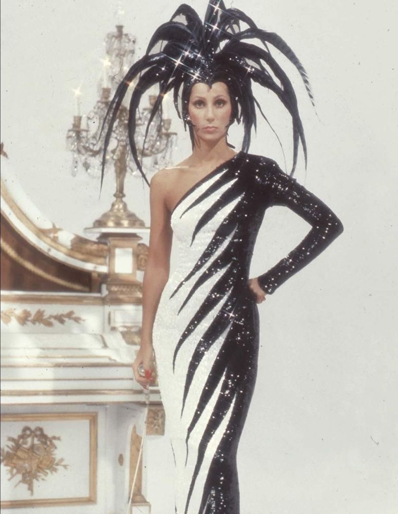 Cher nos anos 1970 em vestido preto e branco, com cabelo com penas