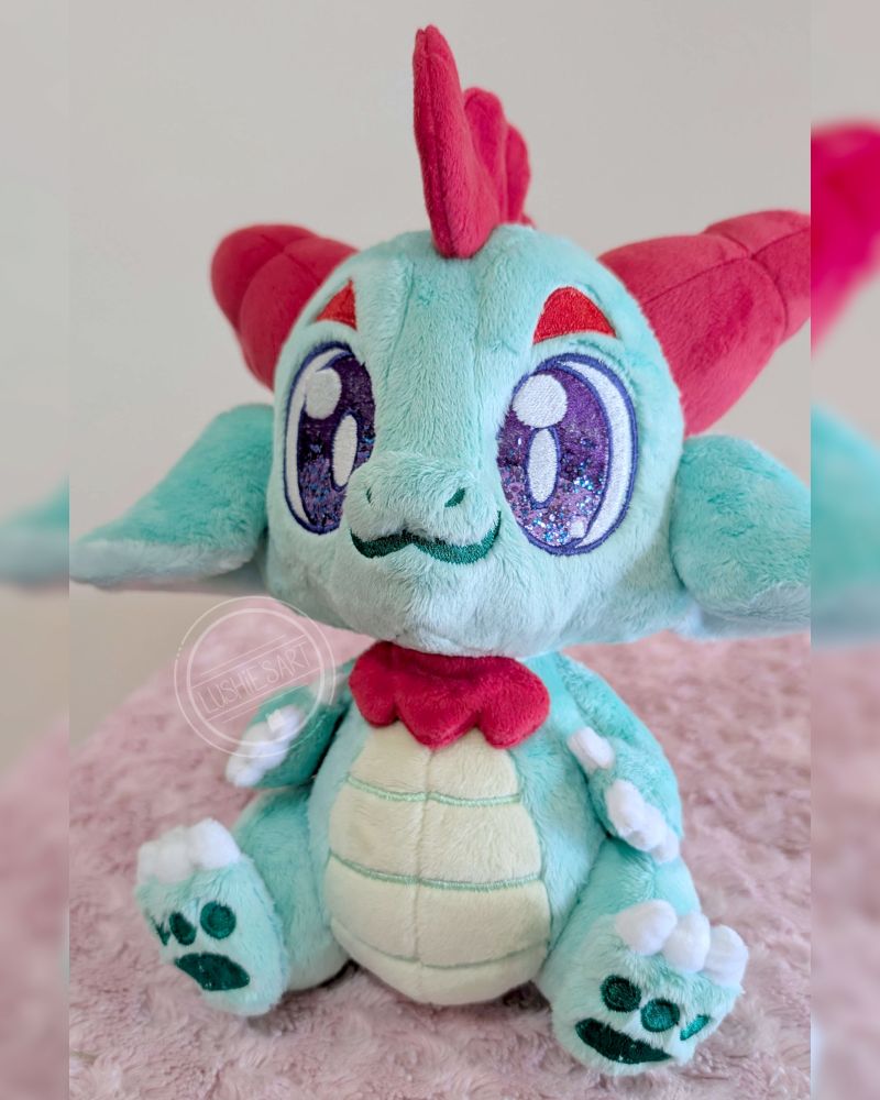 Photo of a green dragon plushie. It has red accents and purple eyes.