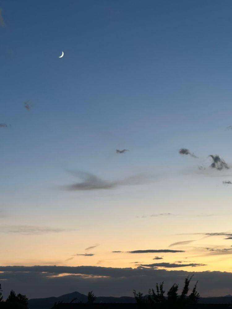 Crescent moon at sunset.  Pale blue and yellow.  Mountain silhouettes 