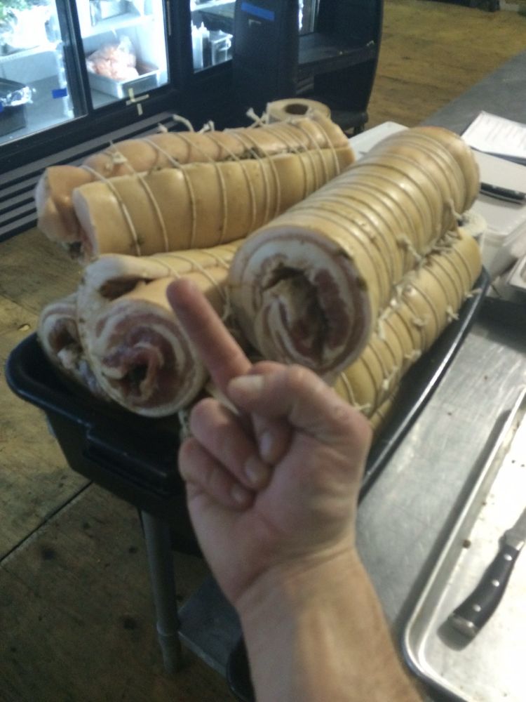 A guy flipping off a bus tub of porchetta. It is late and working all day and still not done.
