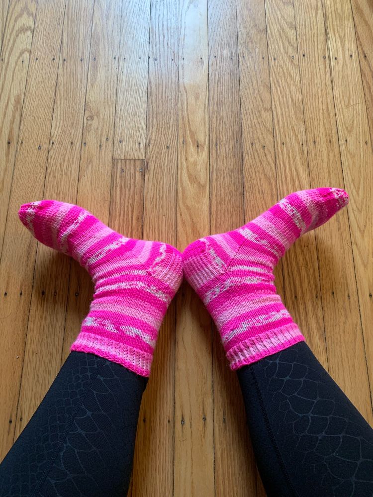 From the knee down, a woman’s legs in black on black python tights and socks made in a five-stripe pattern, all shades of Barbie pink. Wearer’s feet are turned outward in utter glee.