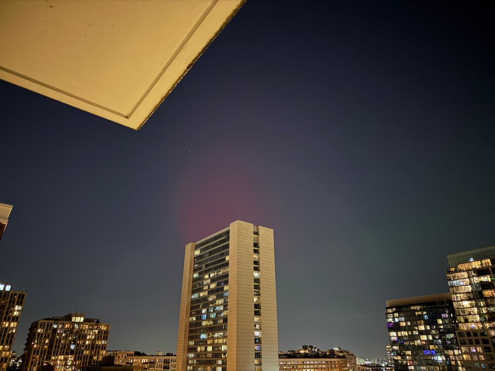 Faint pink and green aurora visible above brightly lit buildings in downtown Chicago. 