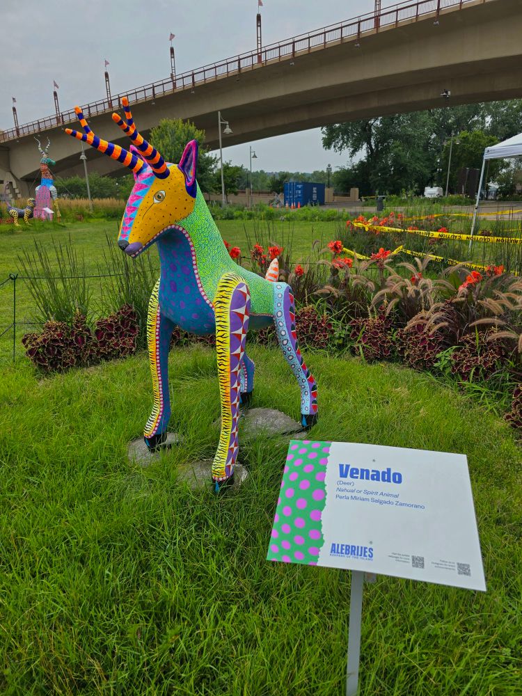 venado: a statue of a deer with bright orange and black horns, a green body, a blue chest, and yellow and purple legs. its face is orange with pink down the middle.