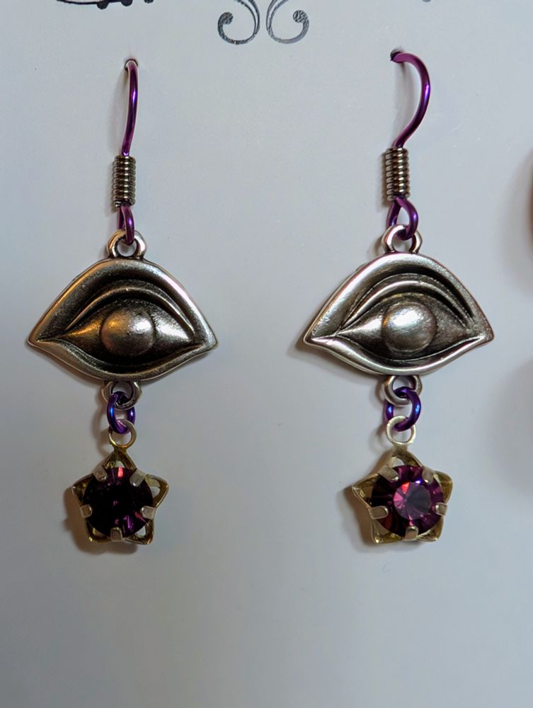 Earrings with silver eyes with a purple gem inside a star hanging from it. 