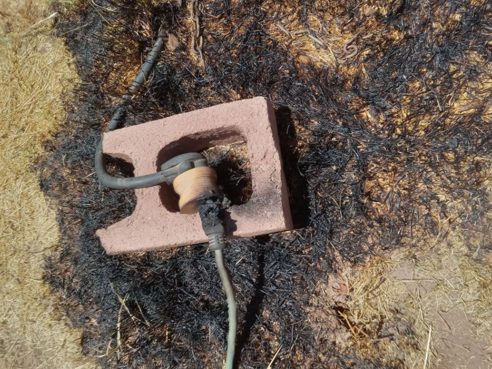 The electric cord to my camp trailer, propped up on a brick. It's visibly melted. The grass around it is burnt.