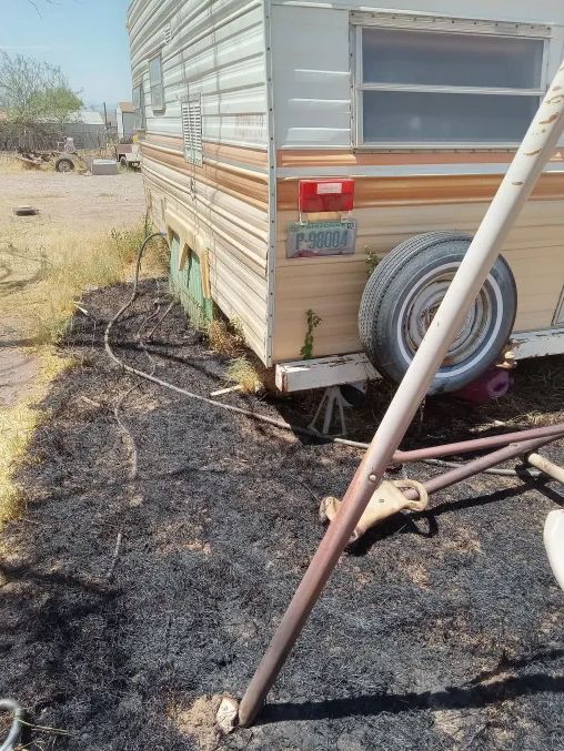A picture of the back of the camp trailer. The grass surrounding it and underneath it is all black from being burnt.