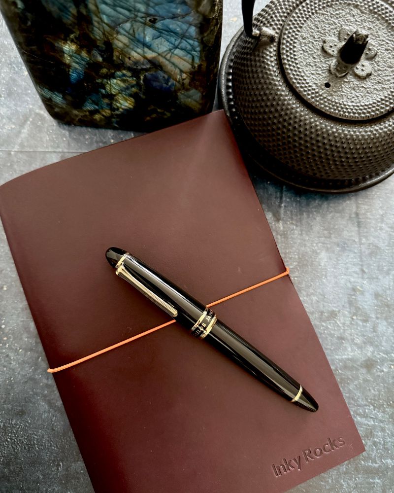 Black and gold Sailor  Crosspointe fountain pen on a Paper Republic journal in the color Venezia. All next to a  Japanese iron teapot and slab of Labradorite 