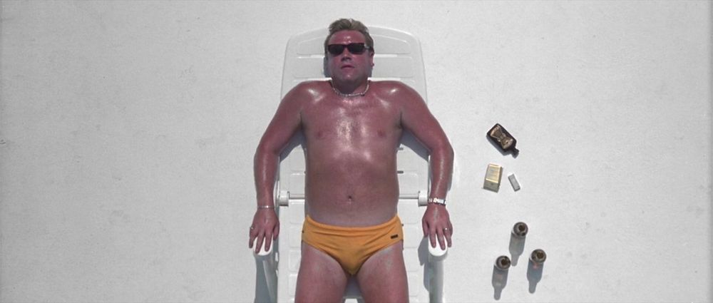 Fotograma de la película Sexy Beast (2000). Muestra a un hombre en speedo amarillo tomando el sol con gafas de sol.