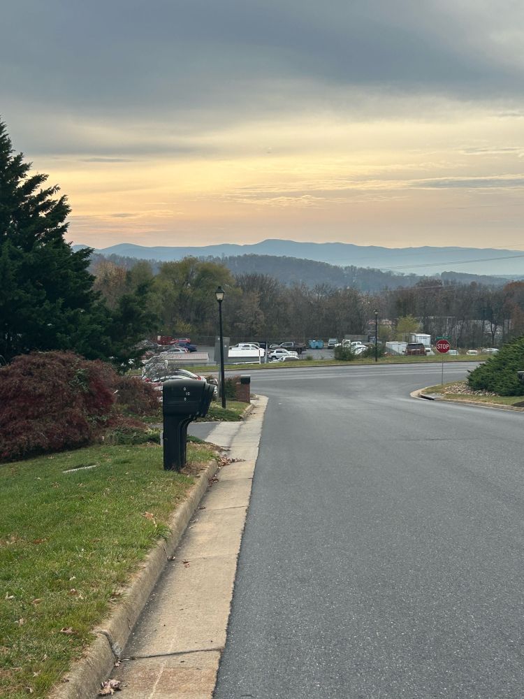 A downhill view showcasing a mountain range under a multicolored sky, with cars visible in a nearby parking lot.