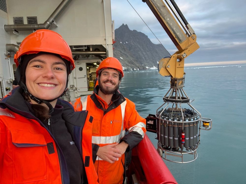 Bryony Freer and Colleague stood on a ship with a CTD instrument being lowered into the water below. 