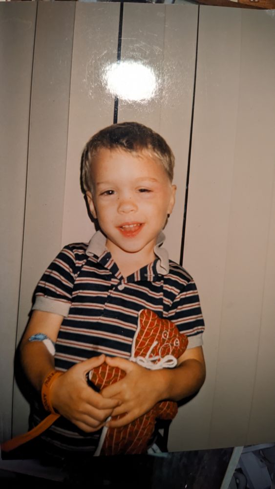 A photo of my old self, at age ten, holding a plaid stuffed bear. An orange hospital bracelet around his right wrist and a gauze bandage around his forearm. He's smiling but he looks more confused than happy. Something is wrong with his left eye: the eyelid droops so low it's almost closed. This is ptosis, a side effect of the barbiturates administered during & after surgery.