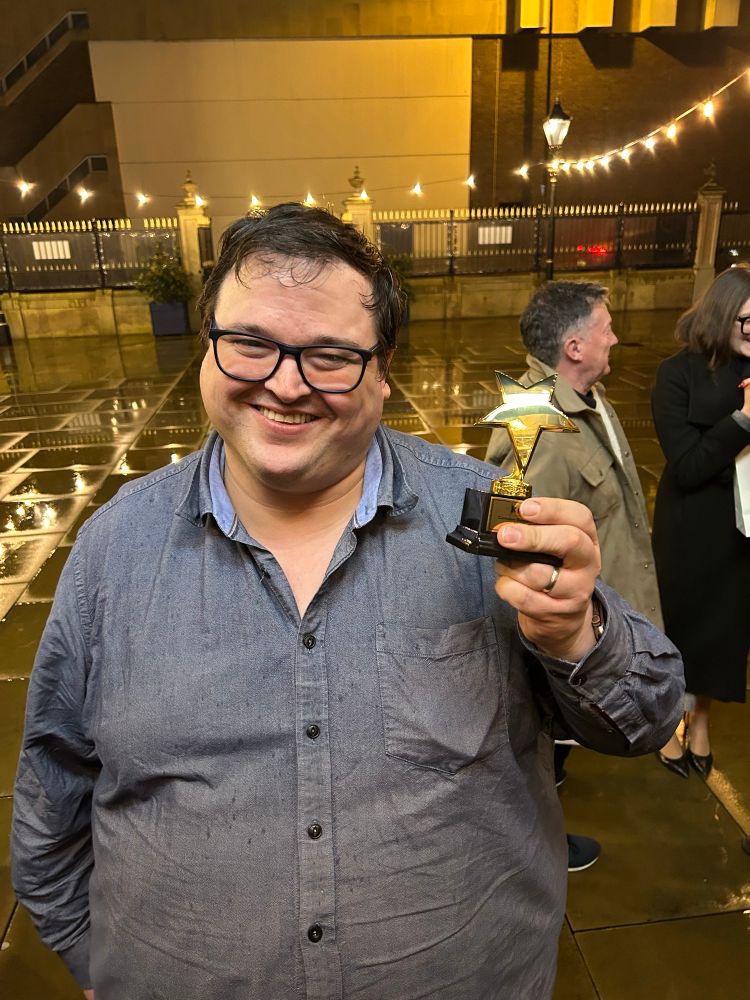 Me in a blue shirt standing in a courtyard holding a small star shaped trophy.