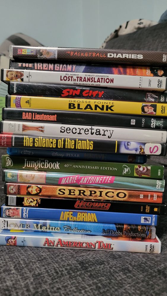A stack of dvd's and blue Rays starting from the top, the basketball diaries, the iron giant Lost in translation Sin City, grosse pointe blank. Bad lieutenant secretary silence of the lambs pixar brave The Jungle Book, Marie Antoinette serpico headwig and the angry inch life of Brian over maine collection in American tale.