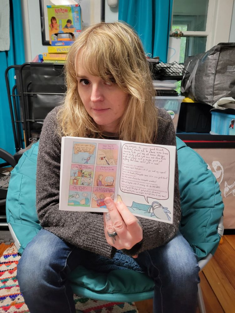 April Landry holding up her zine Liberation Zonked and showing resources and comic