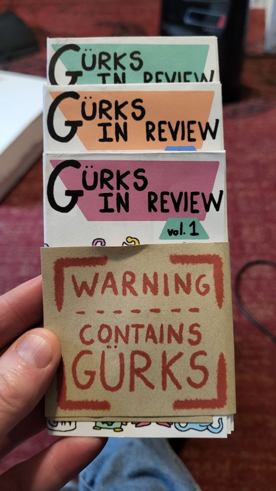 3 volumes of the zine gürks in review, wrapped in a warning label that says warning contains gürks.
