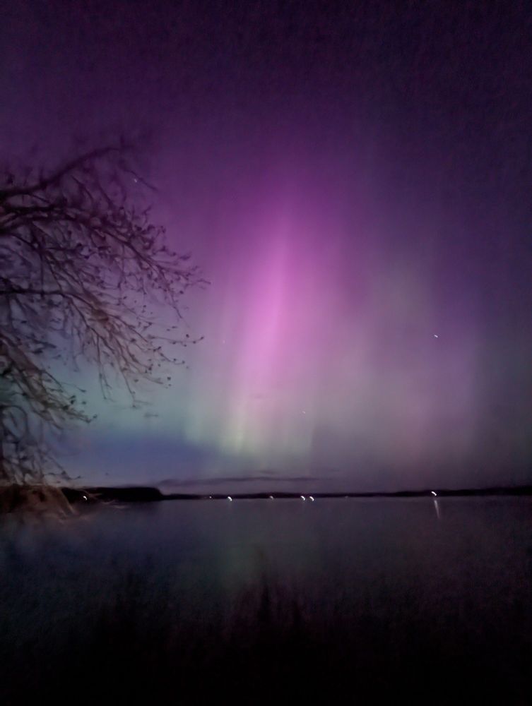 A curtain of pink and green Northern Lights over a lake