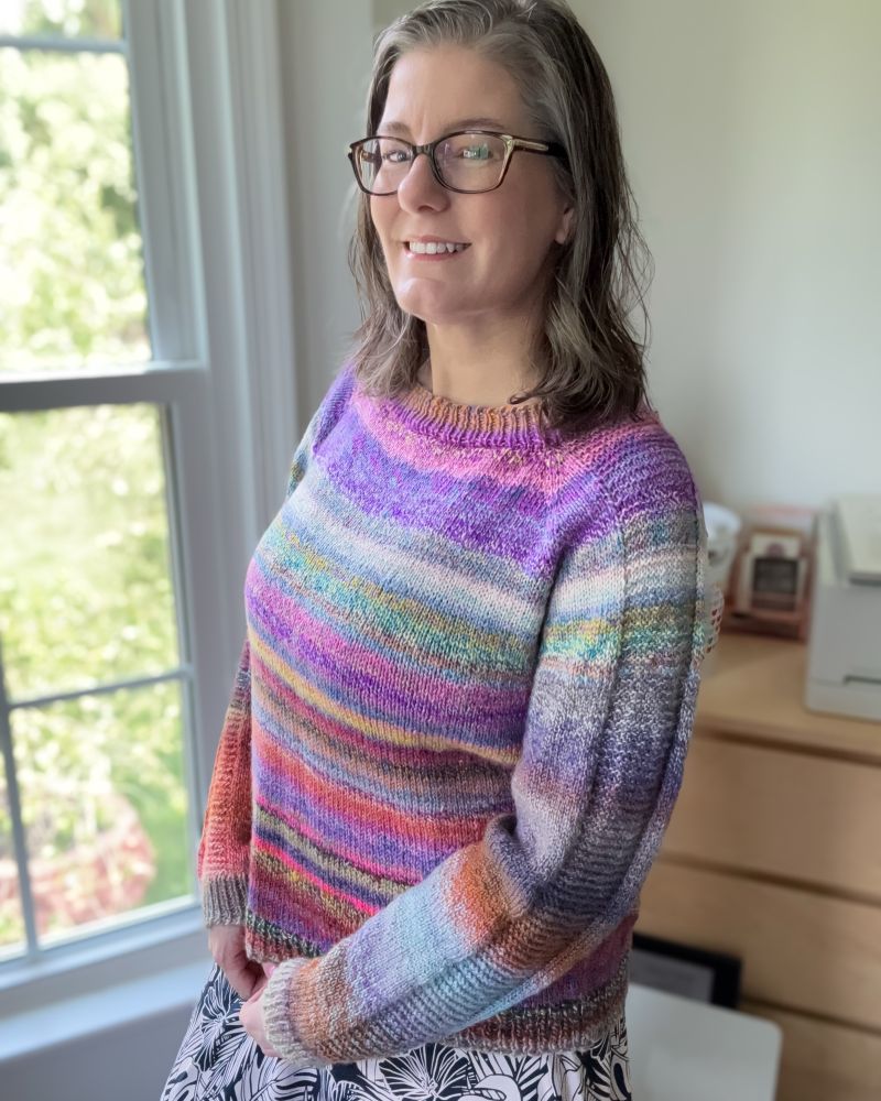 Woman wearing a handknit sweater with garter stitch details on the sleeves. Various gradient colors.