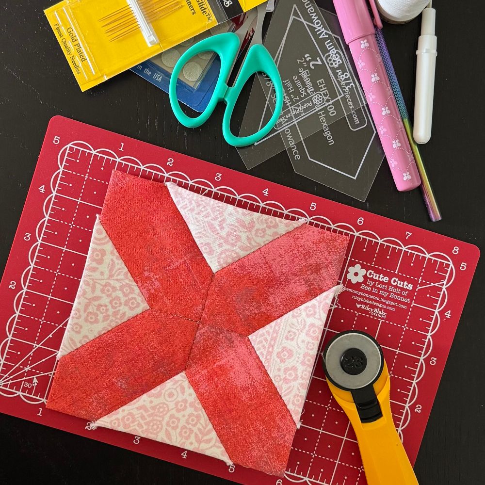 The start of an x shaped English paper piecing quilt block. Fabrics are red and pink.