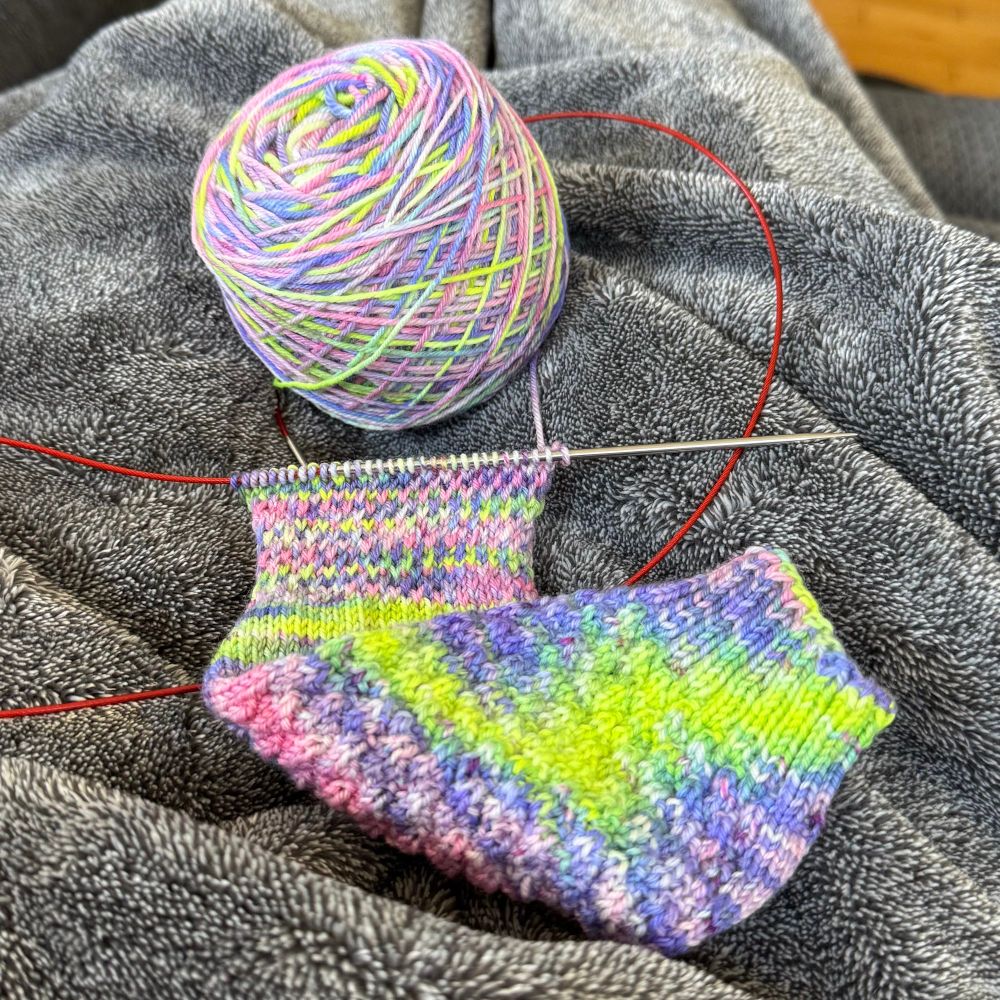 A work in progress handknit sock. The yarn is bright yellow, pinks, and purples