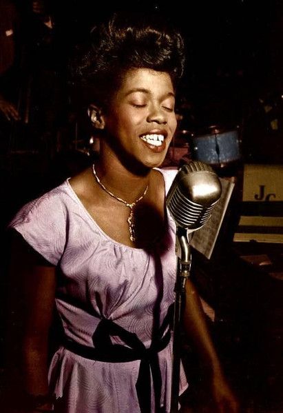 Sarah Vaughan, en una actuación de juventud, gesto sentido frente a un micrófono antiguo, vestido rosa y una elegante gargantilla al cuello. Discogs.