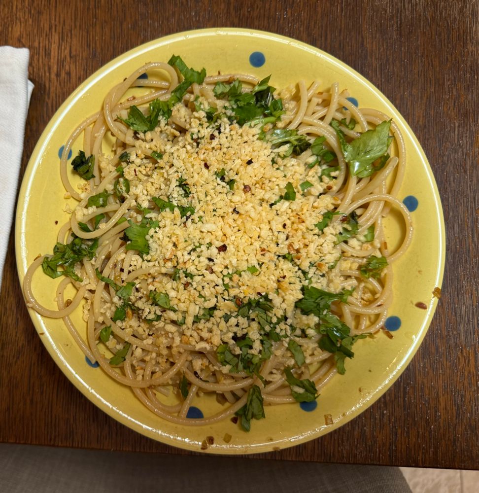 Golden pangrattato and green parsley over thick pasta in a yellow bowl