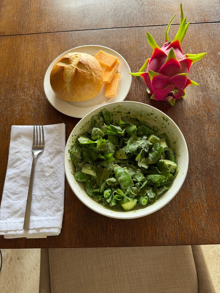 Bright green salad in a white bowl, with a golden brown roll, three slices of orange cheddar, and a pink dragon fruit