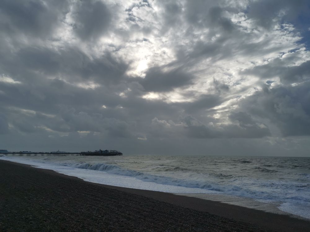 Brighton beach, with pier in background and the sun behind the clouds. 
