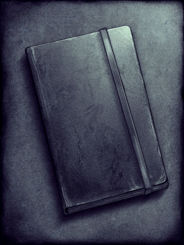 A drawing of a dark greyish blue sketchbook with a strap near the side farthest from the binding. The book is scratched and stained from continual use. The mood of the piece is somber. 