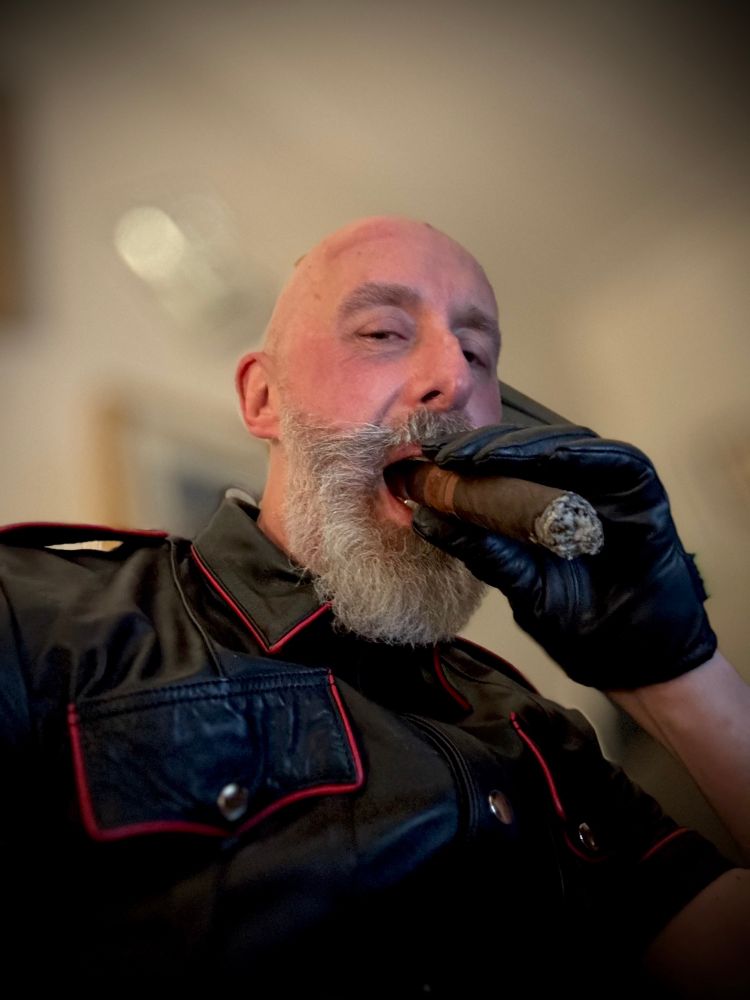 60 year old man,holding a large cigar in a black leather glove up to his mouth, wearing a black leather shirt trimmed in red 